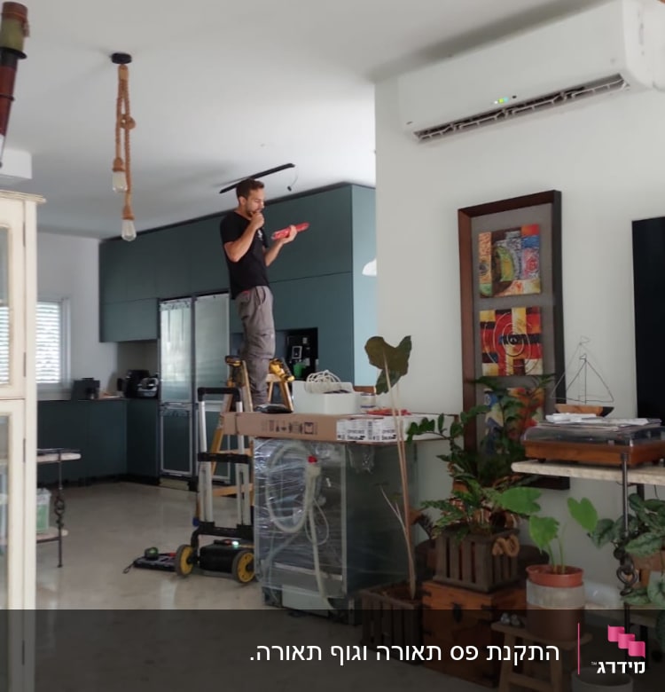 חשמלאי עומד על סולם ומתקן תאורה בתקרה